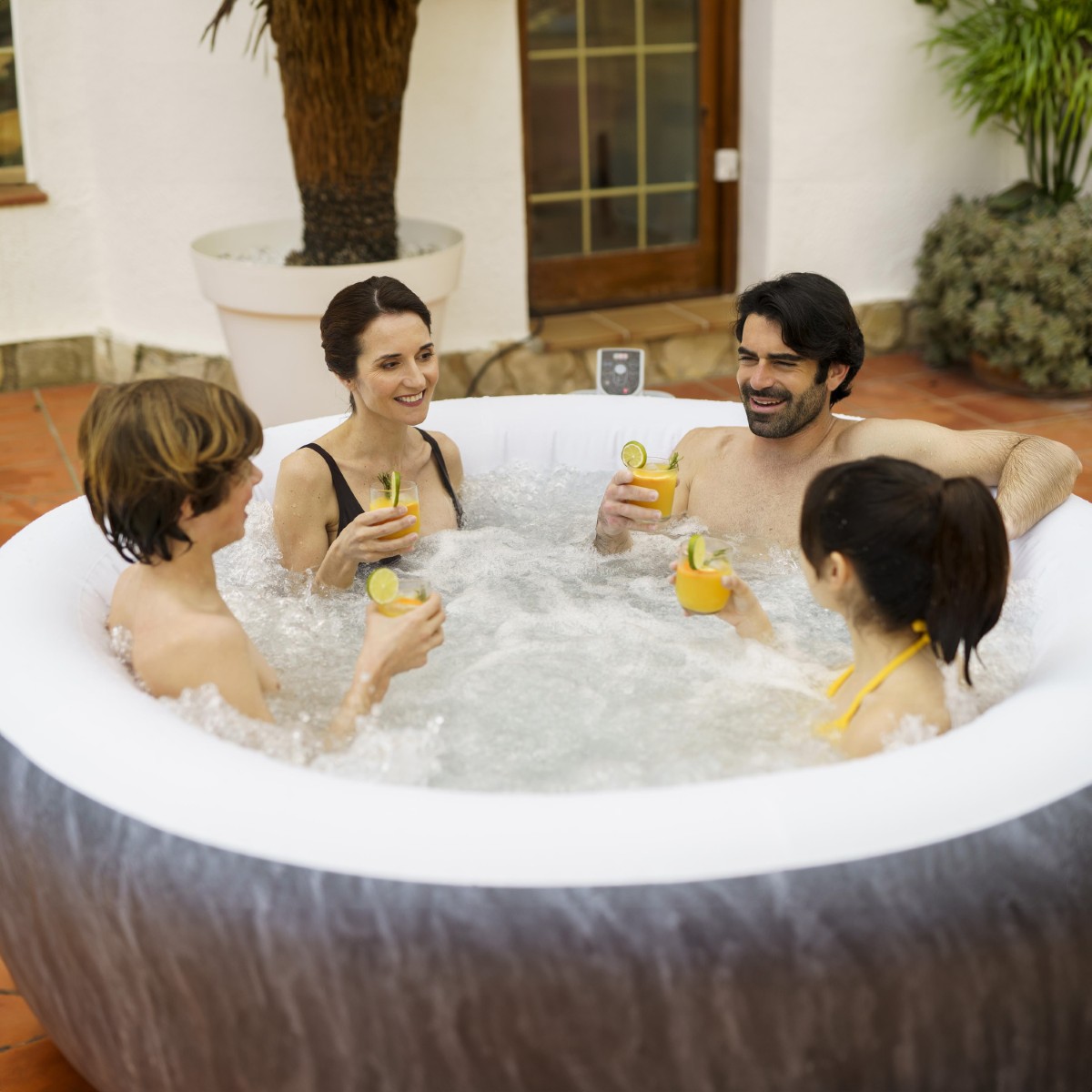 Rodzina w jacuzzi Boracay Smart wznosi toast szklankami z sokiem pomarańczowym. Woda jest spieniona przez działający system dysz powietrznych.